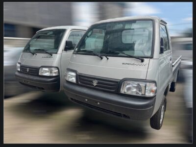 Image 3: Front exterior view of two silver metallic 2026 Suzuki Super Carry pickup trucks highlighting the grille and headlights