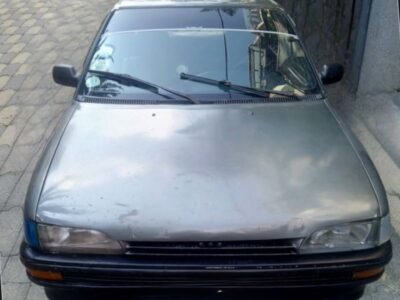 Image 1: Front passenger side angle of 1991 Toyota Corolla XL E90 Woyane sedan in Gray Metallic paint with alloy wheels