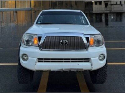2:Direct front profile of white Toyota Tacoma 4x4 showing custom front grille, clear headlights, integrated fog lights, and dark sun-strip